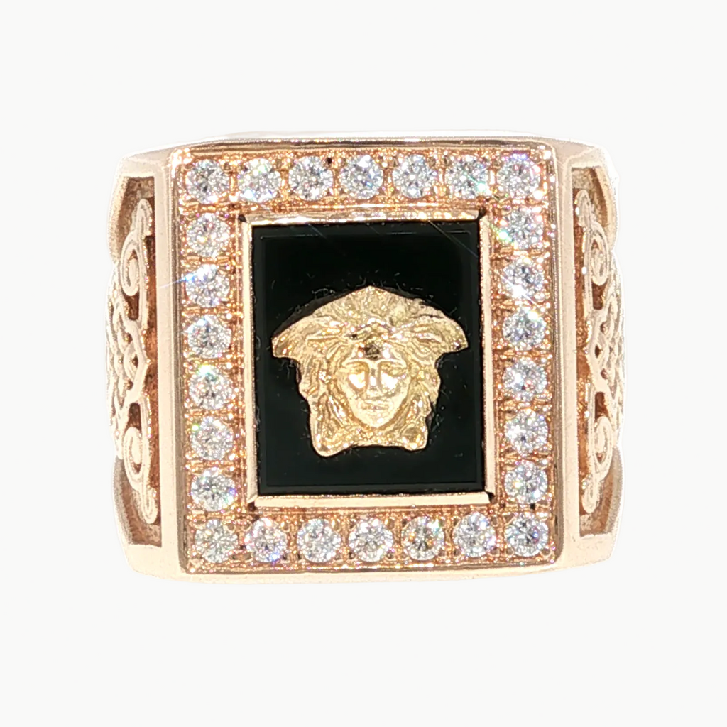 A square rose gold ring featuring a central black inlay with a gold Medusa head, surrounded by a border of clear pavé stones, on a plain white background.