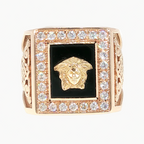 A square rose gold ring featuring a central black inlay with a gold Medusa head, surrounded by a border of clear pavé stones, on a plain white background.