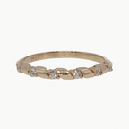 A delicate rose gold band ring featuring small, evenly spaced clear round-cut gemstones, photographed on a clean, light gray reflective surface.