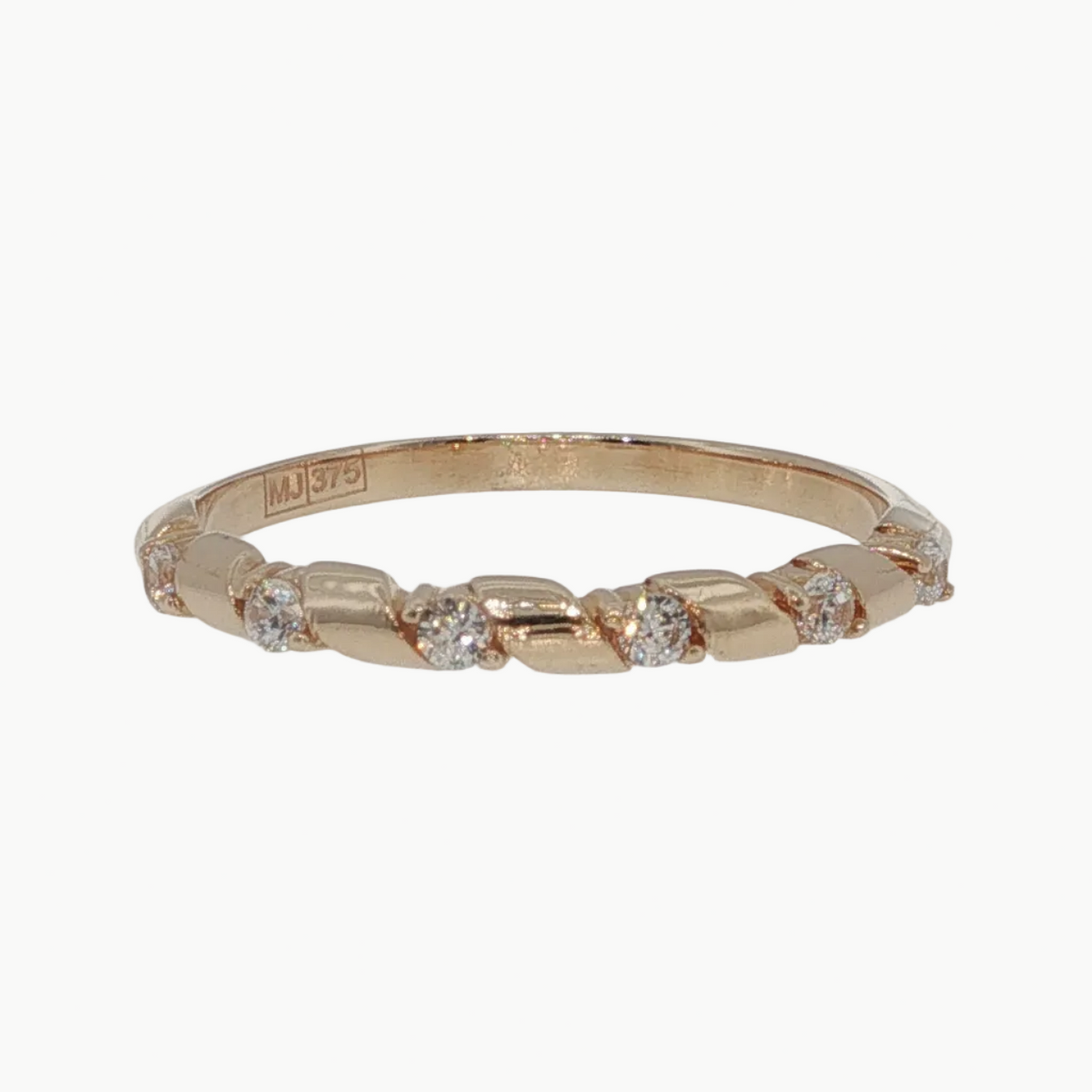 A delicate rose gold band ring featuring small, evenly spaced clear round-cut gemstones, photographed on a clean, light gray reflective surface.