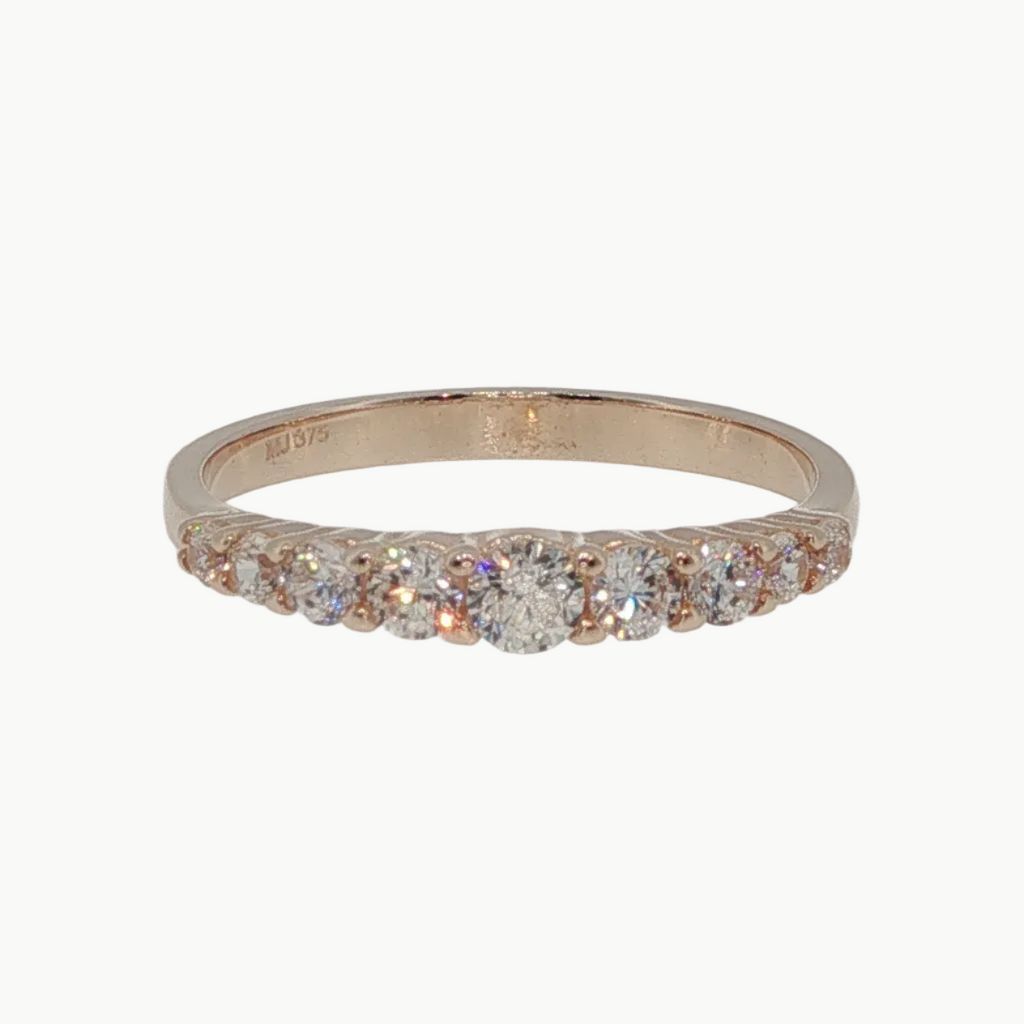 A rose gold eternity ring with a row of clear round-cut gemstones, photographed on a clean, light gray reflective surface.