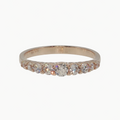 A rose gold eternity ring with a row of clear round-cut gemstones, photographed on a clean, light gray reflective surface.