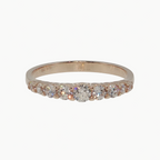 A rose gold eternity ring with a row of clear round-cut gemstones, photographed on a clean, light gray reflective surface.