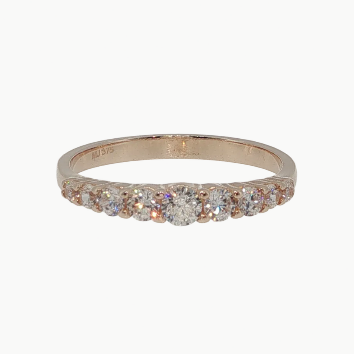 A rose gold eternity ring with a row of clear round-cut gemstones, photographed on a clean, light gray reflective surface.