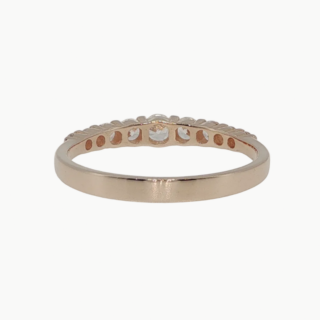 A rose gold eternity band ring with a row of small round-cut clear stones, photographed on a clean white reflective surface.