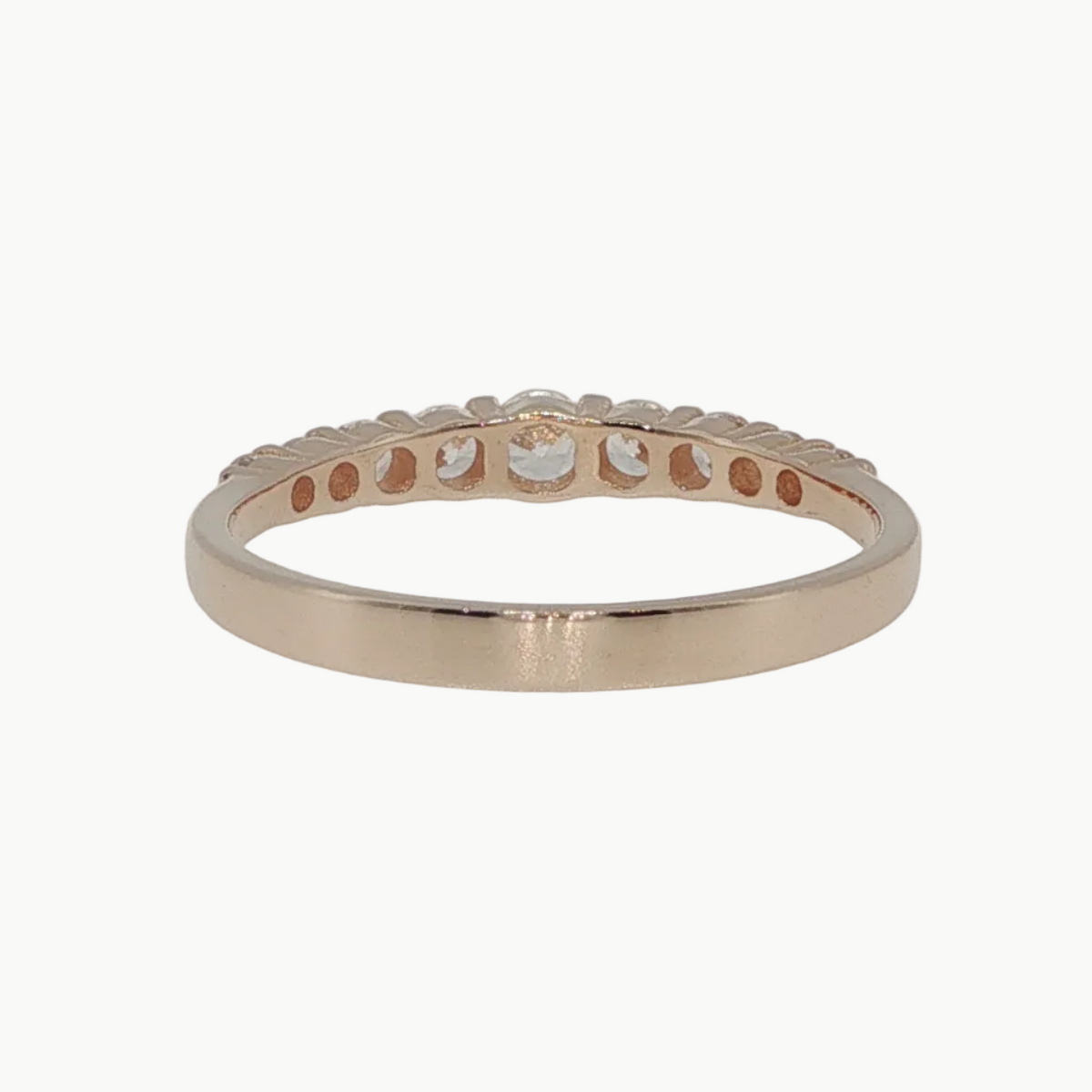 A rose gold eternity band ring with a row of small round-cut clear stones, photographed on a clean white reflective surface.