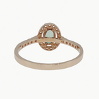A rose gold ring with a central oval cluster of small clear stones and a marquise-cut green gemstone in the middle, shown on a light gray background.